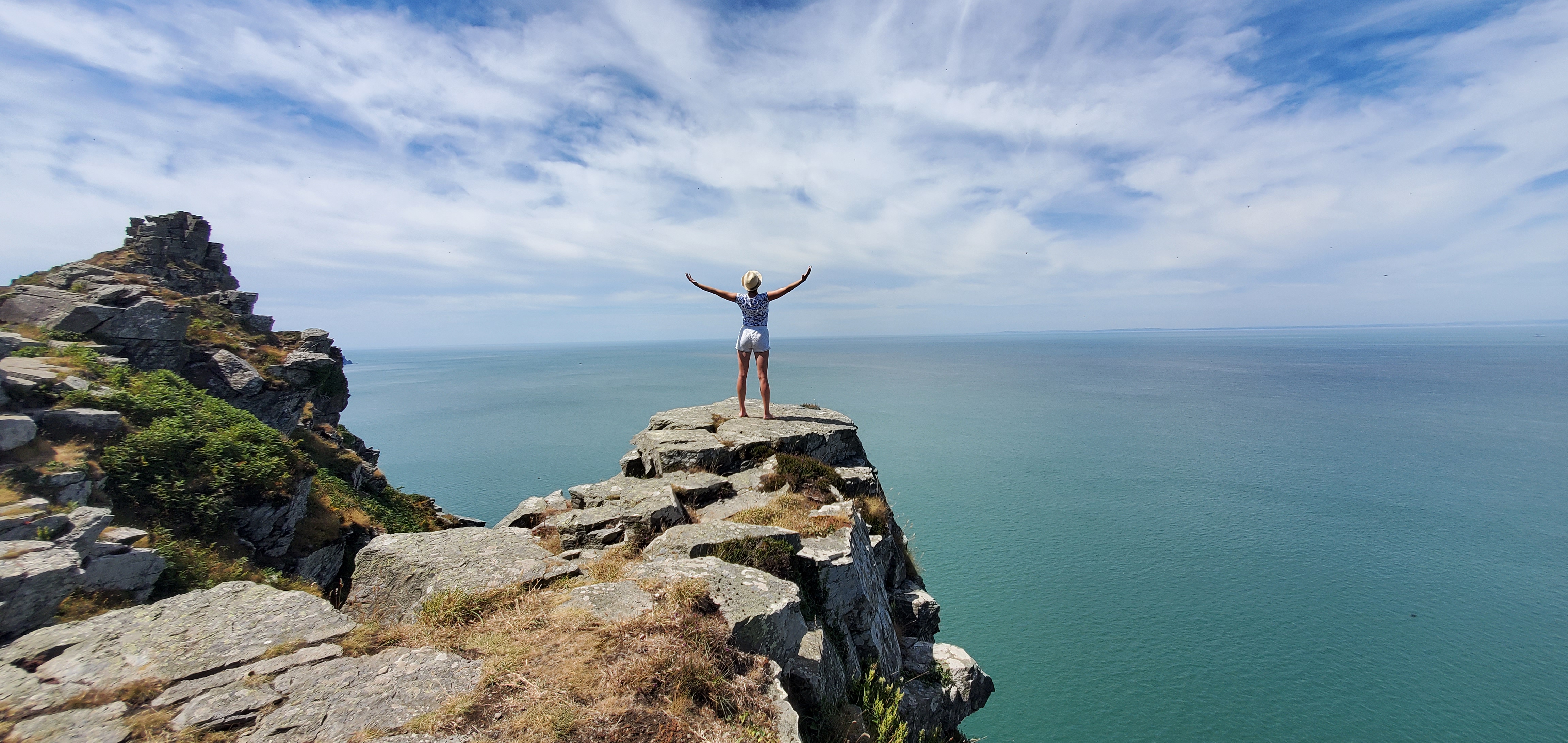 A woman standing on a clifftop above the sea with her arms open to the sky